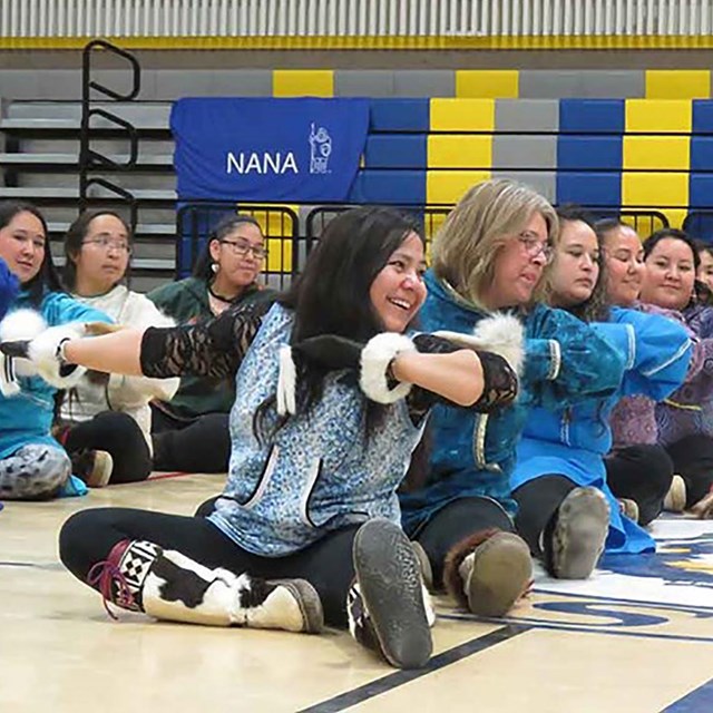 A group of woman site on floor as part of a dance performance.